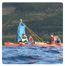 Image of adults and children in a full canoe raft, with an improvised sail rigged up