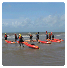 image of a group of people pulling their sit on top kayaks across the beach to the edge of the sea