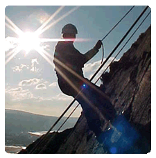 Boy abseiling silhouetted with sun behind as he stops to have his picture taken