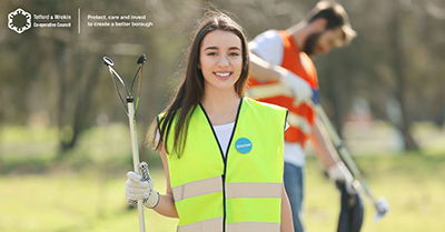 A picture of a women in a park, holding a litter picker and a black bag, taking part in the Great British Spring Clean.