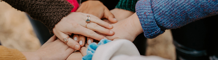 A photo showing a group of people placing their hands in a circle