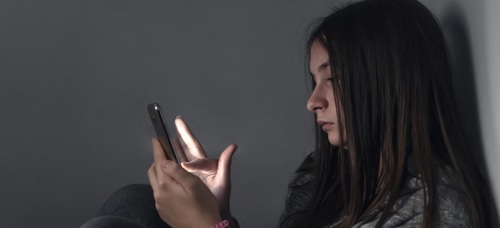 A teenage girl sitting in a corner looking on their mobile phone