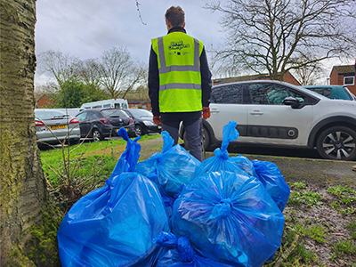 A picture of a Street Champion standing behind a bunch of blue bags filled with litter.