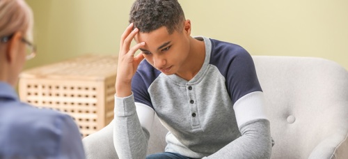 A teenage boy holding his head in his hand listening to an adult explain their options