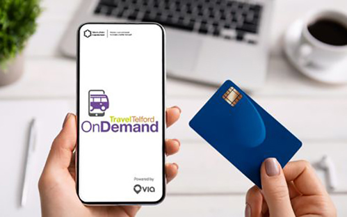 A picture of someone holding a mobile phone in their left hand and a credit card in their right hand, booking a bus journey through the Travel Telford on Demand app.