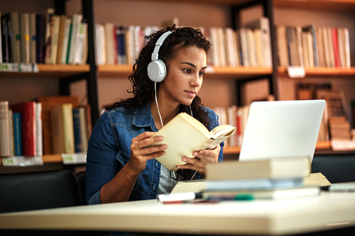 Picture of a young female student studying in the library. She is using a laptop and learning online.