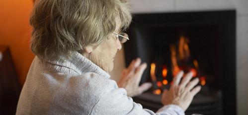 Senior woman warming hands by fire at home
