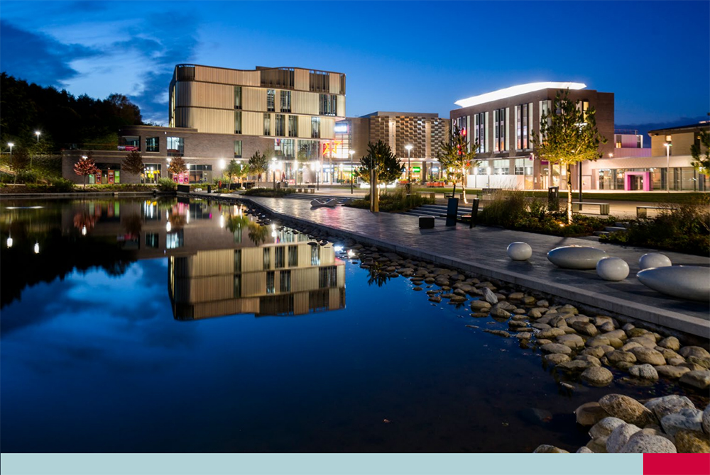 Modern buildings at Southwater, Telford Town Centre illuminated at dusk, with reflections in the water and landscaped surroundings.