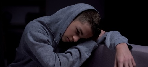 A youth in a hoodie sitting on a sofa looking worried