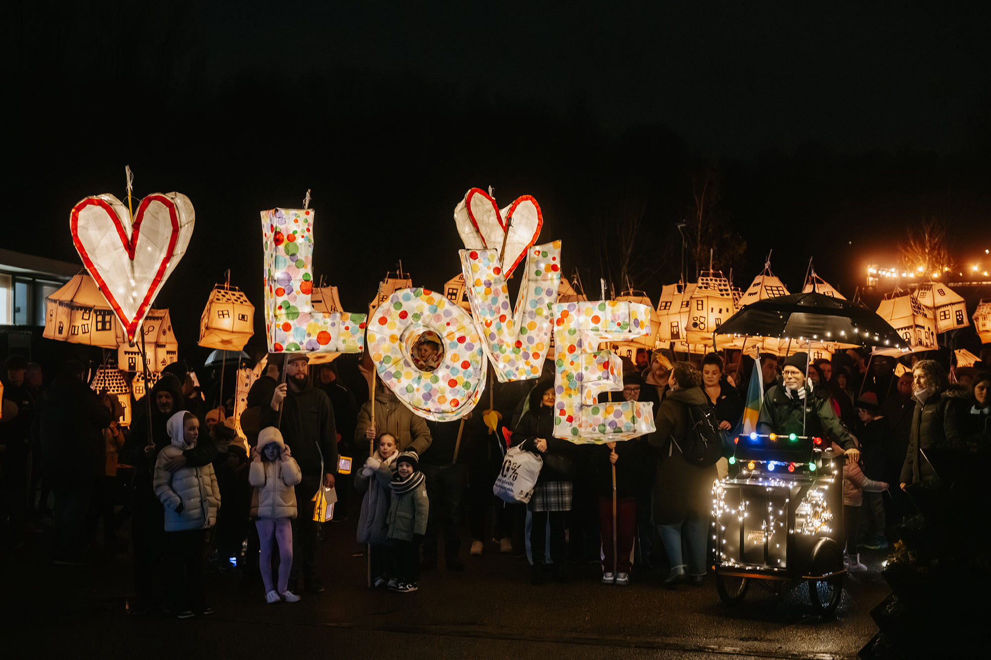 A lantern parade at Telford Day 2025, with community members carrying illuminated lanterns shaped like houses and large lit letters spelling “LOVE” between two heart shapes.