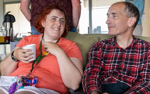 A picture of a male and female sitting on a settee, while drinking a cup of tea and having a chat.