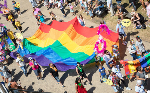 A photo of a large pride flag carried by people attending a pride parade