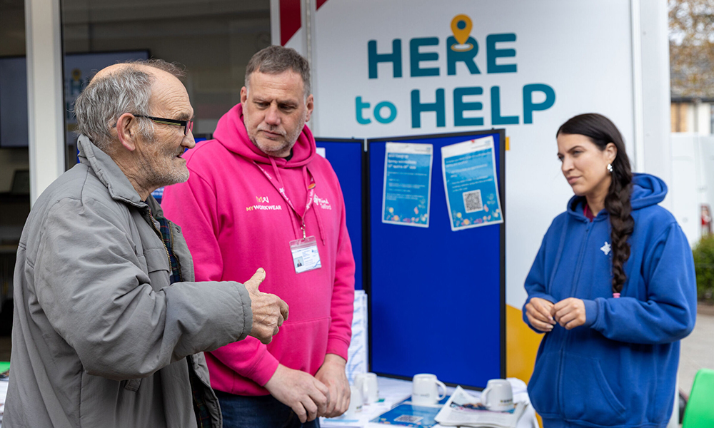 A photograph showing two Here to Help colleagues engaged in conversation with a gentleman, providing guidance and support.