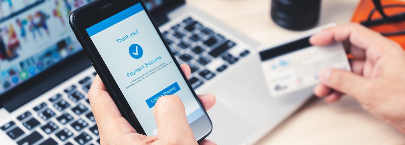 Online shopping concept, hands holding using smartphone for mobile internet banking with credit card for making payment transaction with laptop on table