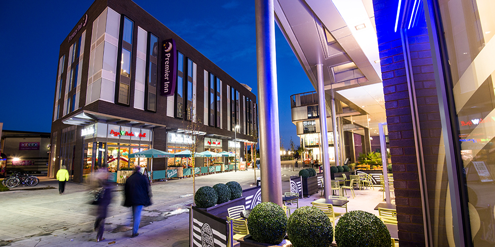 Southwater in Telford at night, showing illuminated shops, restaurants and outdoor seating areas with pedestrians walking through the town centre.