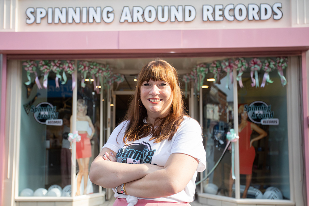 Person standing outside Spinning Around Records in Newport with folded arms, in front of the shop entrance and display windows.