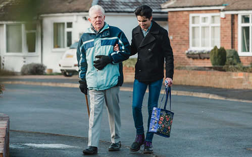 Teenage boy is walking back from the shop with his grandparent.