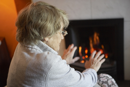 Senior woman warming hands by fire at home.