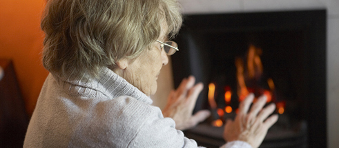 Senior woman warming hands by fire at home.