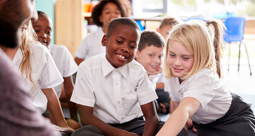 Male teacher reading story to a group of school children wearing uniform in school classroom