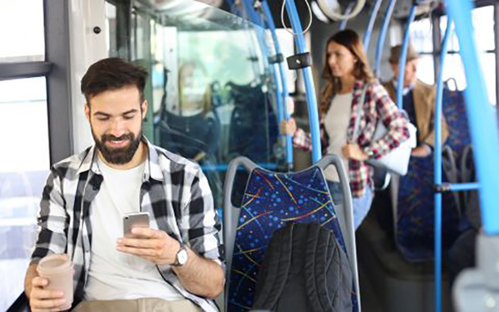 A picture of a man, sitting on a bus, looking at his mobile phone.
