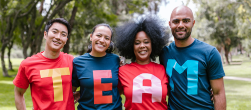 A photo of four people in a park each wearing a t-shirt with a letter on to form the word TEAM