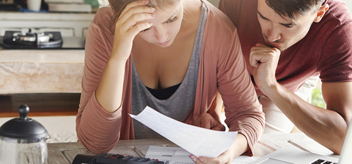 Young couple calculating their domestic budget together in kitchen, trying to save money for buying new car, having stressed and frustrated looks. Unhappy woman showing unpaid bill to her husband