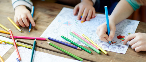 A photo of children using pencils for colouring in a sheet of paper