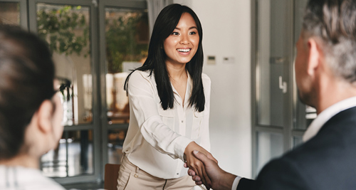 Picture of a woman entering a room for an interview with two interviewers sitting at a desk