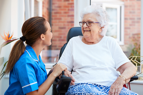 Senior woman sitting In motorised wheelchair talking with nurse In retirement home.