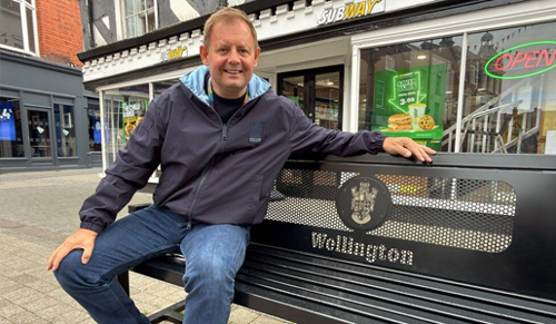 A picture of Councillor Paul Davis sitting on one of the new benches in Wellington Town Centre.